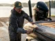 Cleaning Boat Hulls to Stop Invasives: A Full Gear Guide Angler in Simms gear cleaning the hull of a Ranger bass boat with a Mercury outboard at a boat ramp.