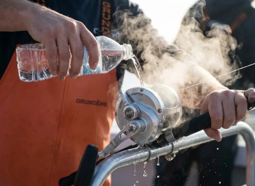 A deckhand in Grundéns bibs pouring water on a hot, steaming Avet HX Raptor lever drag reel attached to a G. Loomis rod.