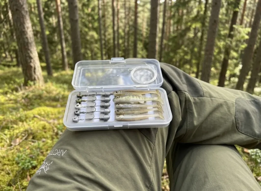 Curated selection of swimbait jigheads in a small travel tackle box resting on a hiker's knee.