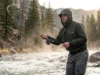 Current Seams Hydrodynamics: The Angler’s Physics Guide Angler wearing Simms waders and Patagonia jacket standing in a turbulent river holding a Sage fly rod.