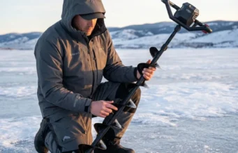 DIY Ice Auger Blade Sharpening Care & Field Repair A professional angler in Simms gear inspecting a Strikemaster ice auger at sunrise on a frozen lake, highlighting technical competence and premium equipment.
