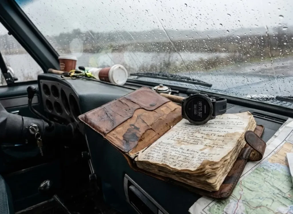 Worn leather fishing journal on a truck dashboard next to a Garmin fēnix 7 watch during rain.