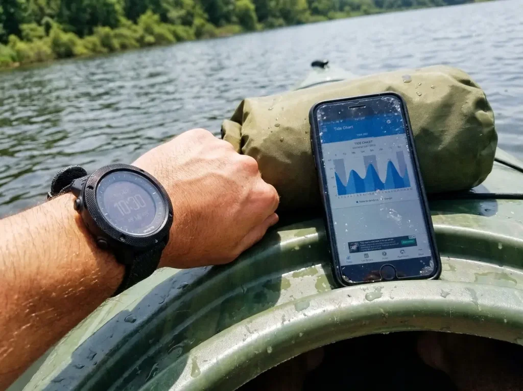 A Suunto Traverse Alpha on the wrist next to a phone tide app, showing the watch-versus-app choice