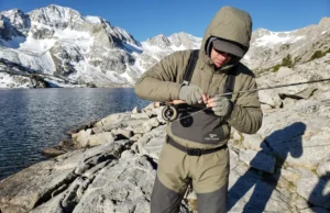 High Altitude Fishing Physics: Technical Field Manual Angler rigging fishing gear at a high-elevation alpine lake surrounded by granite peaks and snow.