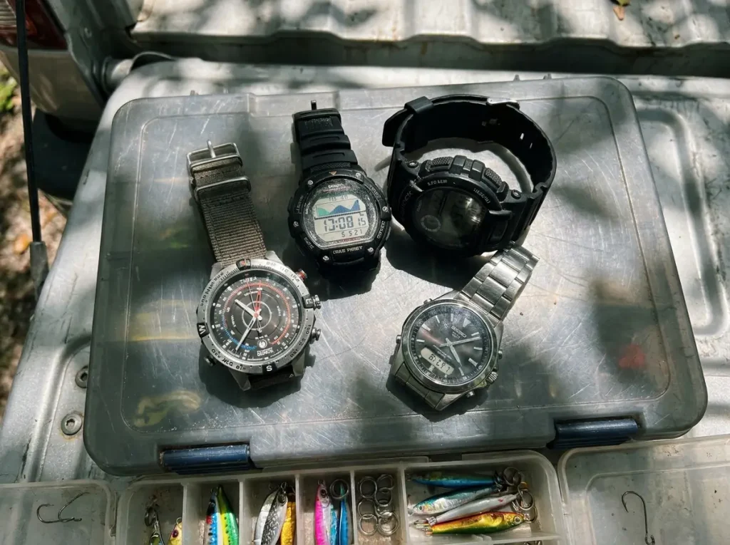 Several fishing tide watches laid out on a tackle box for a buyer's guide comparison