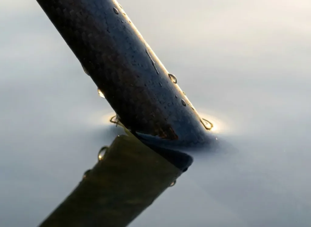 Close-up detail of a carbon fiber push pole silently entering the water, illustrating the stealth required in the hydrodynamic flats environment.