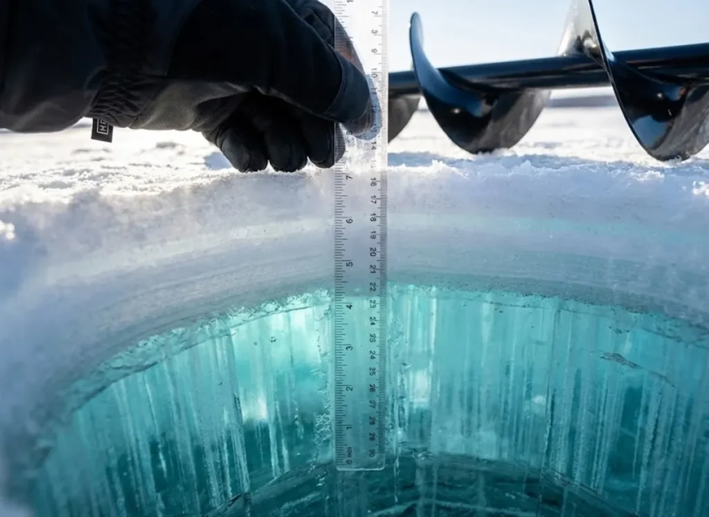 Close up of an ice fishing hole showing the difference between white ice and clear blue columnar ice layers.