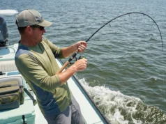 Knot Strength Physics: Friction & Mechanics for Anglers A fisherman leans back with a deeply bent rod, straining against a heavy fish, highlighting the tension on the fishing line and knot.