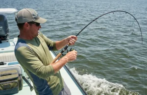 Knot Strength Physics: Friction & Mechanics for Anglers A fisherman leans back with a deeply bent rod, straining against a heavy fish, highlighting the tension on the fishing line and knot.