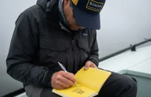 Logbook Maintenance Data: A Complete Audit Guide Angler writing in a Rite in the Rain notebook wearing Patagonia gear while fishing in foggy conditions.