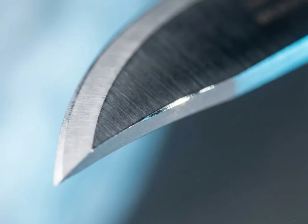 Extreme macro close-up of a steel ice auger blade edge showing microscopic geometry and light reflecting off a dull spot for diagnosis.