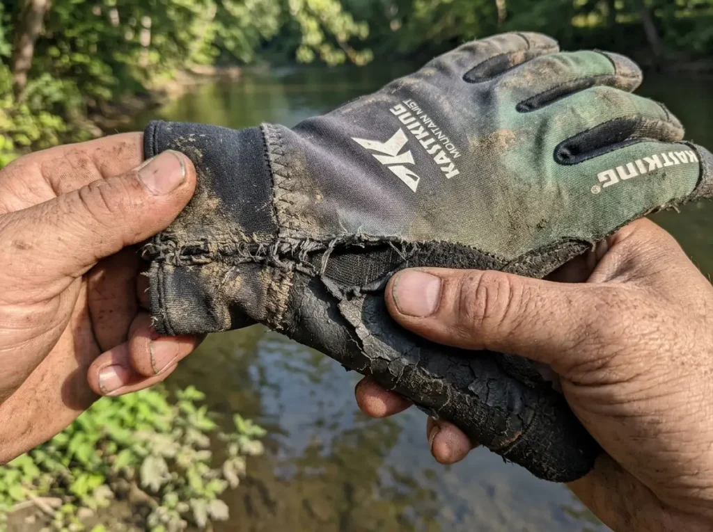 Worn noodling glove showing a peeling palm coating and stressed wrist seam after a season