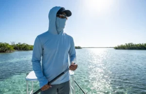 The Physics of Glare: Polarized Sunglasses Axis for Anglers Professional angler on a skiff poling platform wearing polarized sunglasses, backlit by harsh midday sun with intense glare reflecting off the tropical water surface.