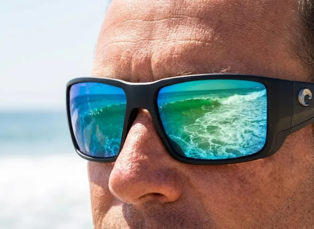 Extreme close-up of an angler wearing Costa Del Mar polarized sunglasses, with the reflection of breaking waves and deep troughs visible in the lenses.