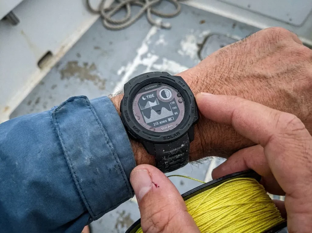 Close-up of a Garmin Instinct 2 Solar Surf showing tide and moon data on an angler's wrist