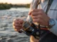 Removing Line Memory Coils: Field & Home Fixes Angler fixing coiled fishing line memory on a Shimano Stella spinning reel while wearing a Patagonia shirt.