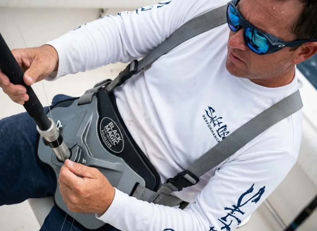 Angler using a Black Magic Equalizer harness and Oakley sunglasses to shift leverage during a big game fight.
