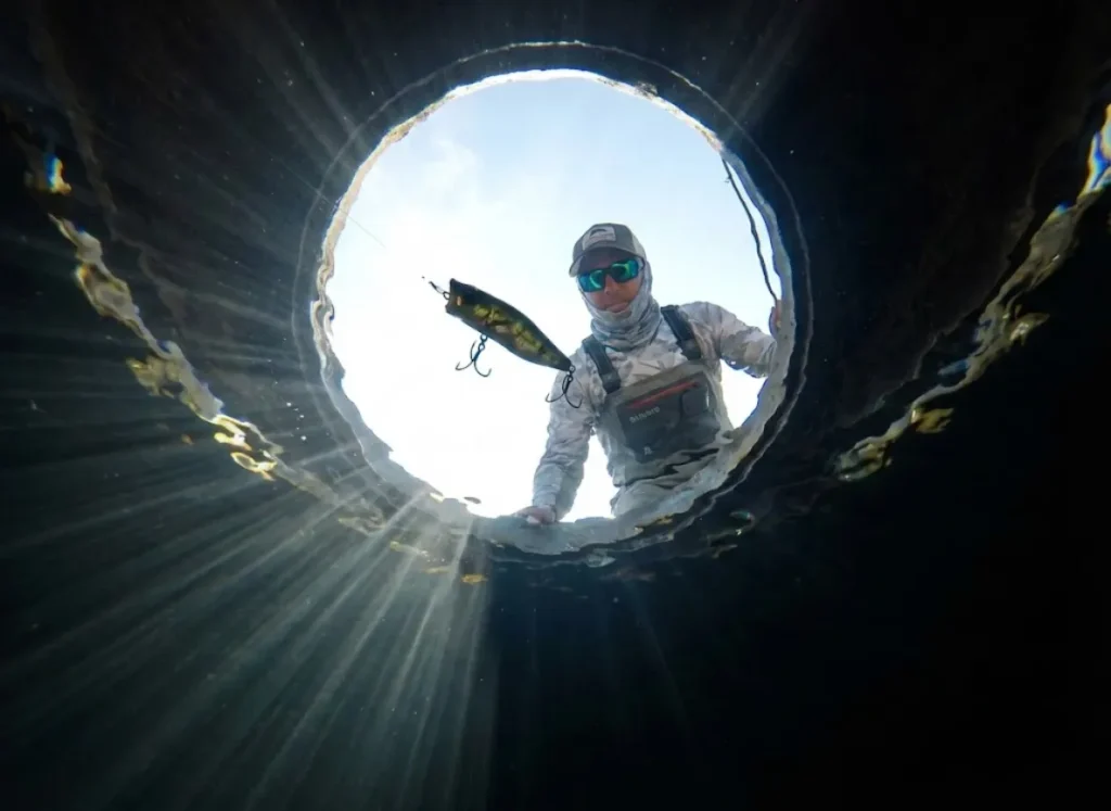 Underwater view looking up at a Megabass lure and an angler in Costa sunglasses distorted by Snell's Window and surface ripples.