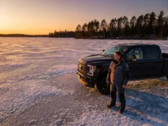 Static Load Bearing: Ice Thickness Safety Physics A professional angler in Simms gear standing next to a truck on a frozen lake at sunset, illustrating ice thickness safety.