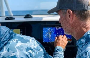 Stop Data Clutter: A Strategic GPS Waypoint Management Guide Angler on a boat wearing Simms and Patagonia gear attempting to navigate a cluttered Garmin GPSMAP screen covered in sea spray.