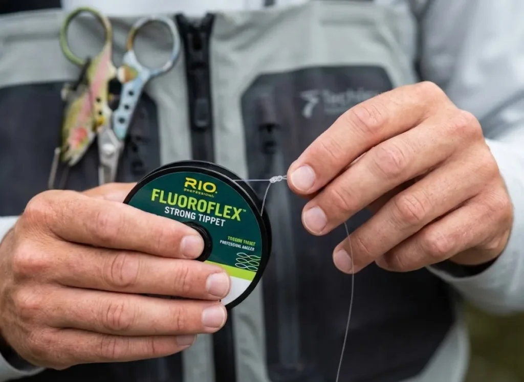 Macro shot of angler hands holding Rio Fluoroflex tippet spool and tying a knot.
