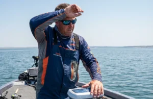 Thermoclines Explained: Fishing Depth & Sonar Guide Angler on a boat in summer heat studying fish finder sonar for deep water layers.