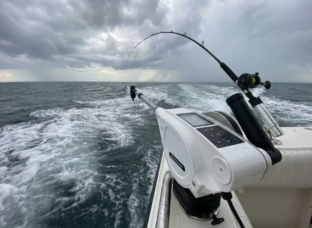 A trolling rod bowed over in a rod holder next to an electric downrigger, signaling a fish is on the line.