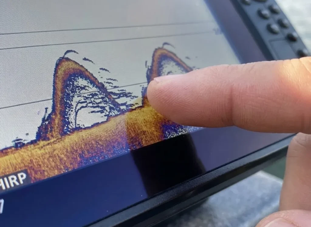 Extreme close-up of a finger touching a high-definition fish finder screen showing clear target separation of fish arches.