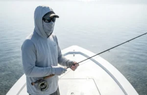 UPF Clothing Physics Protection: The Angler’s Guide Angler on a skiff wearing a Simms SolarFlex hoody and Costa del Mar sunglasses facing intense solar reflection on the flats.