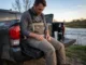 Wader Repair Guide: Patching Leaks for Longevity Angler sitting on a truck tailgate inspecting Simms G3 Guide Waders for leaks with a tube of Gear Aid Aquaseal nearby.