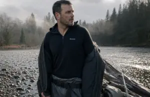 Merino vs Synthetic Fishing Base Layer System Angler in a merino base layer under an open wading jacket at a cold river before fishing