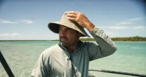 Fishing Hat Sun Protection Features Guides Check First Angler in a wide-brim UPF hat checking fishing hat sun protection features on shallow water