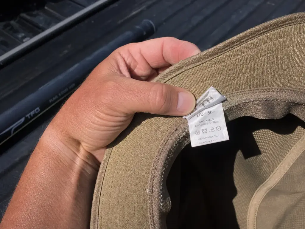 Angler reading the printed UPF 50 rating tag inside a fishing sun hat