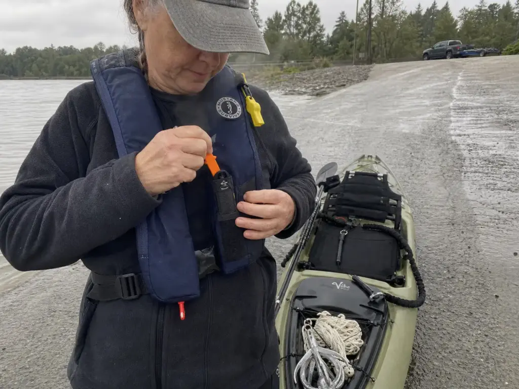 Kayak angler checking the line cutter on her PFD before launching to anchor