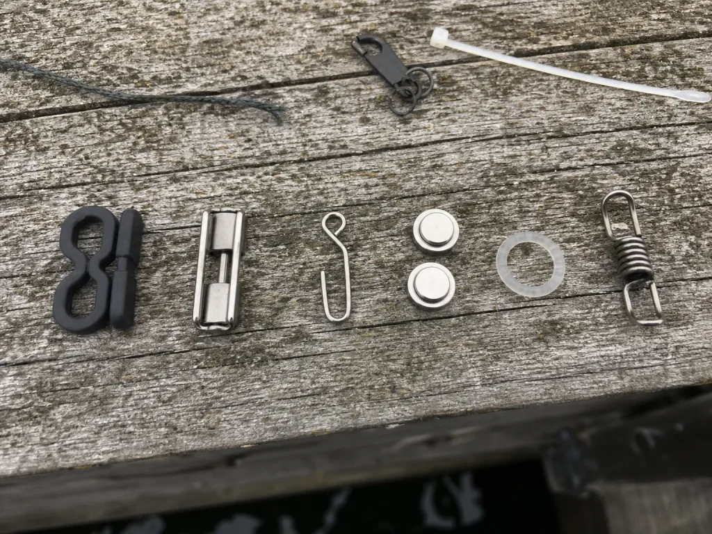 Several types of fishing rod hook keepers laid out on a dock board showing standard, magnetic and silicone designs