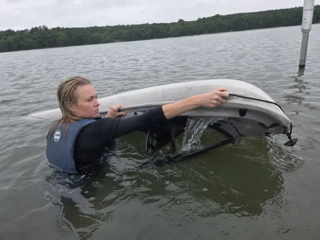 Angler reaching across an upturned kayak hull to grab the far deck line and roll it upright