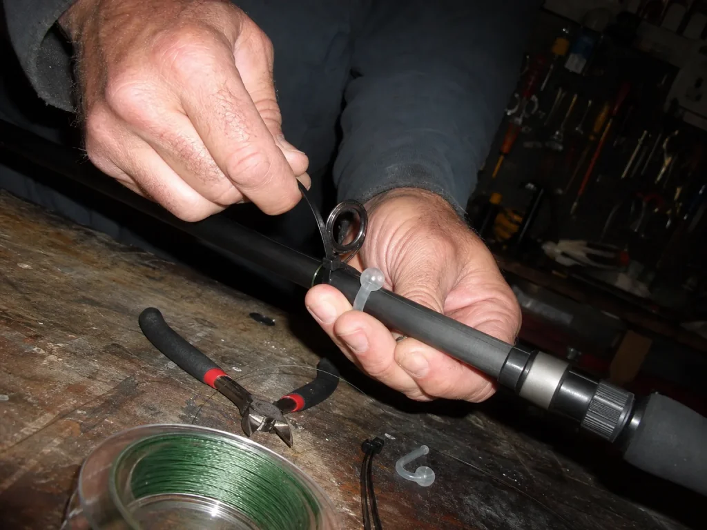 Hands building a DIY hook keeper with a zip tie and split ring next to a silicone universal keeper on a workbench