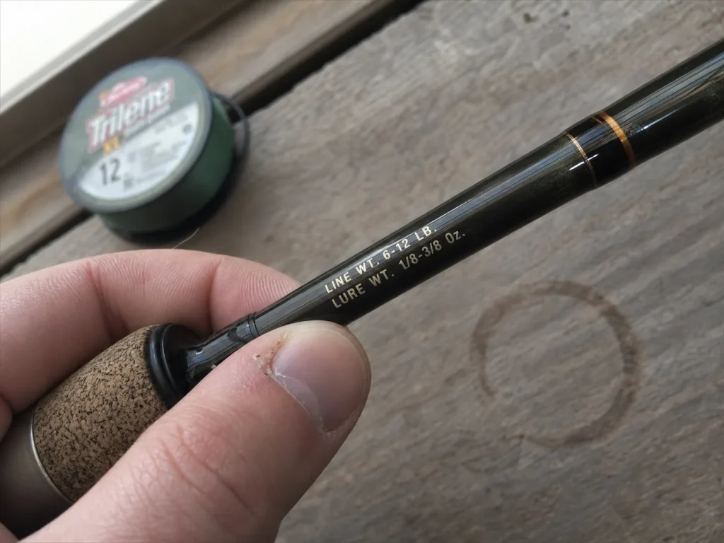 Close-up of the printed line rating and lure weight range stamped on a fishing rod blank near the handle