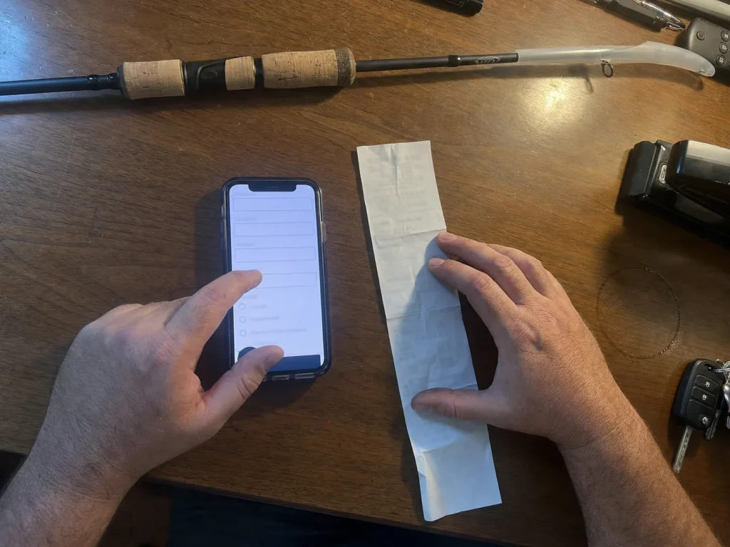 Hands registering a new fishing rod warranty on a phone next to a paper receipt