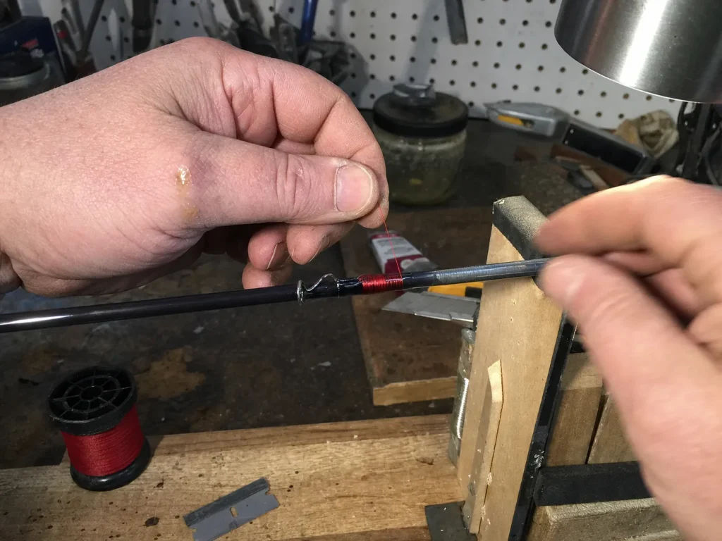 Hands re-wrapping a guide with thread on a rod blank, a modification that can void warranty