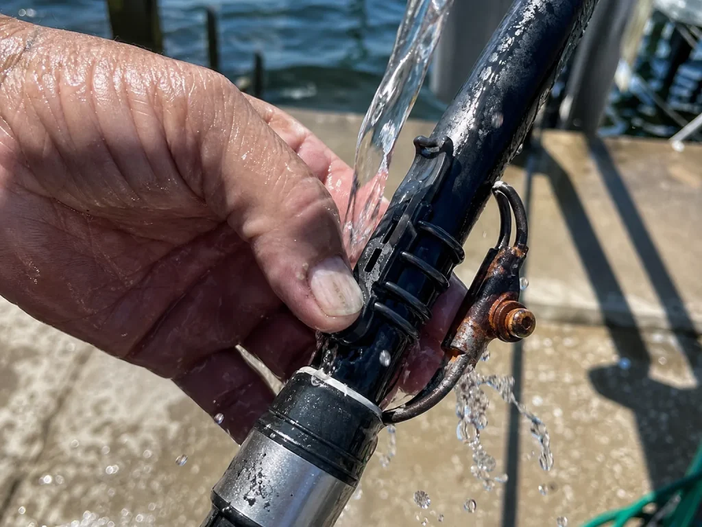Rinsing a reinforced saltwater hook keeper on a rod under fresh water to prevent corrosion after a coastal trip