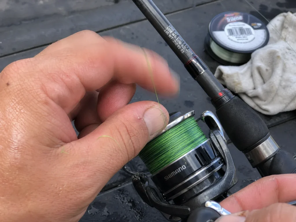 Bright green braided line being spooled onto a spinning reel seated on a rod with a printed line rating
