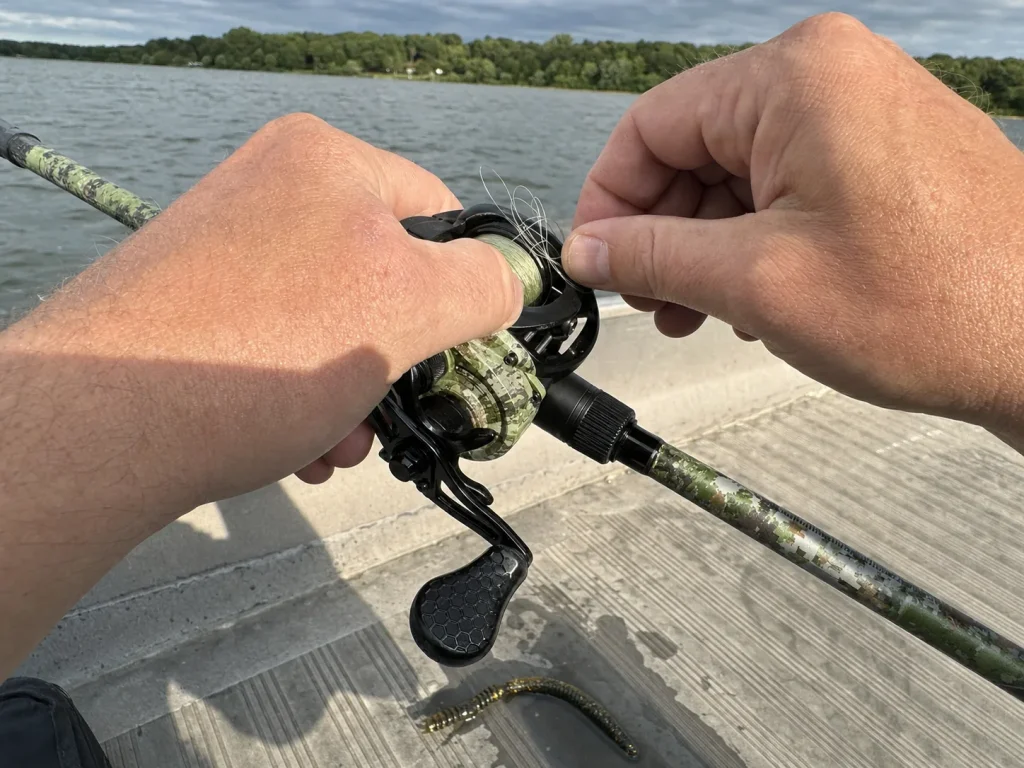Thumb riding the spool of a baitcaster reel while picking out a small backlash on the deck
