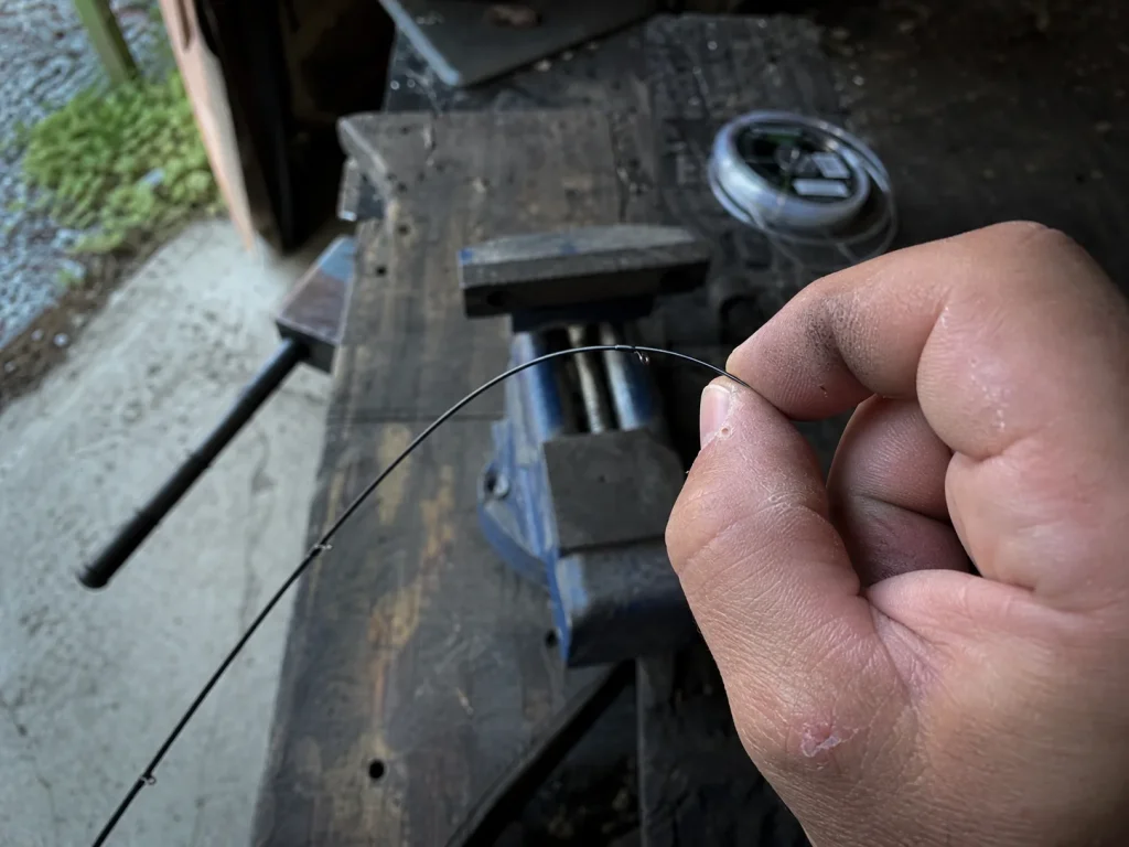 Close-up of a slim high-modulus graphite rod tip flexed under a fingertip showing its thin brittle build
