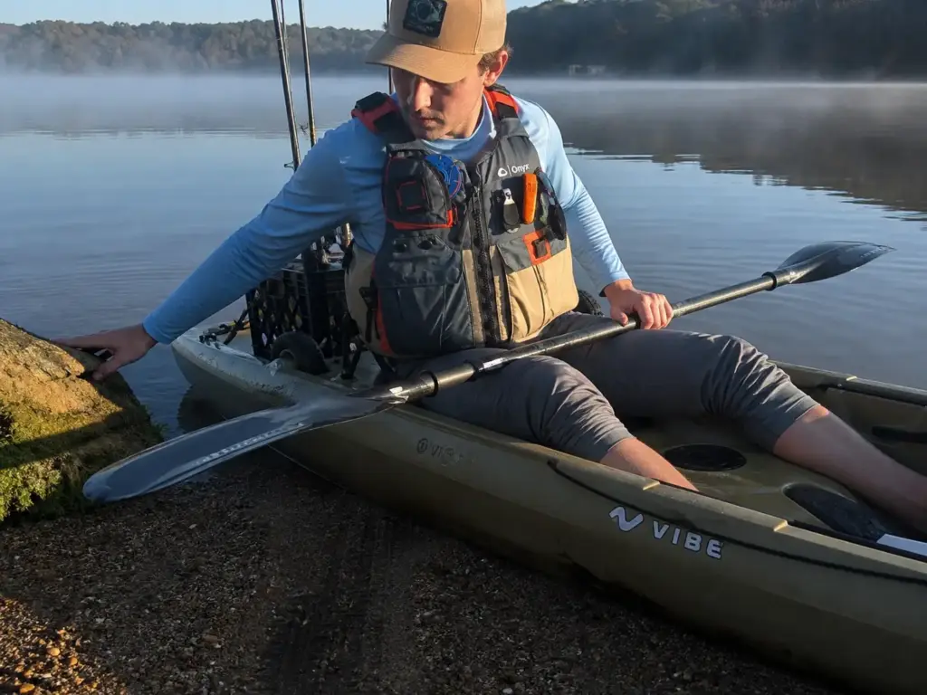 Angler wearing a tan kayak fishing PFD while launching, vest zipped and pockets loaded