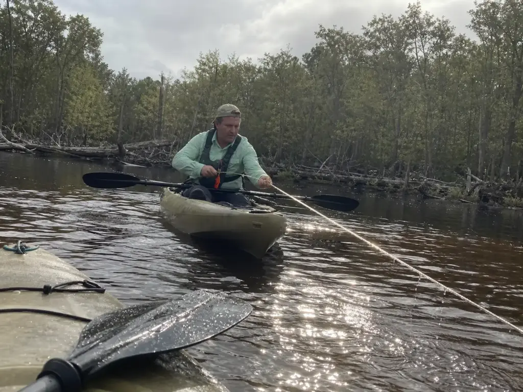 Angler paddling upstream over a stuck kayak anchor to change the pull angle