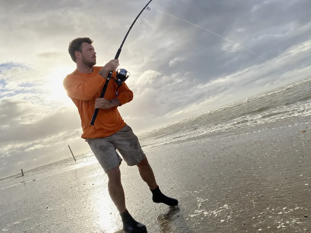 Surf angler fighting a crosswind with a long rod, showing how wind changes the rod length rule