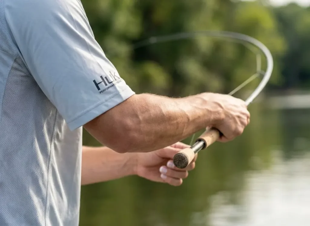 Close-up of an angler's wrist and forearm executing a backhand roll cast with a loaded fishing rod.