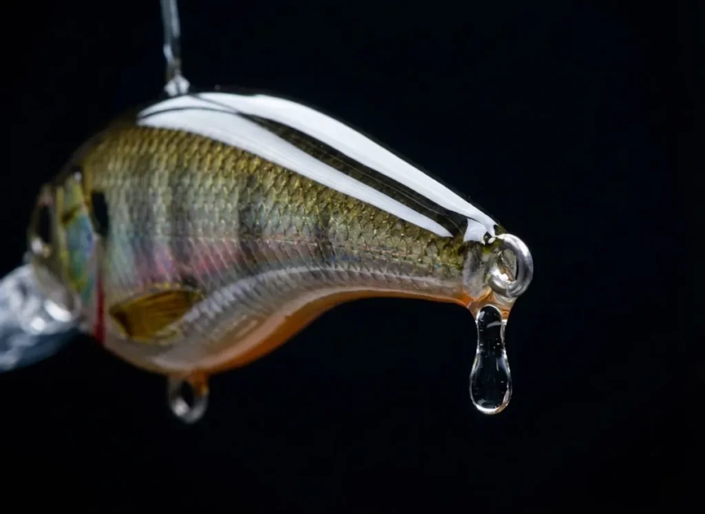 Macro shot of a wet, clear-coated fishing lure hanging to cure, showing a glass-like finish and a droplet of resin at the tail.