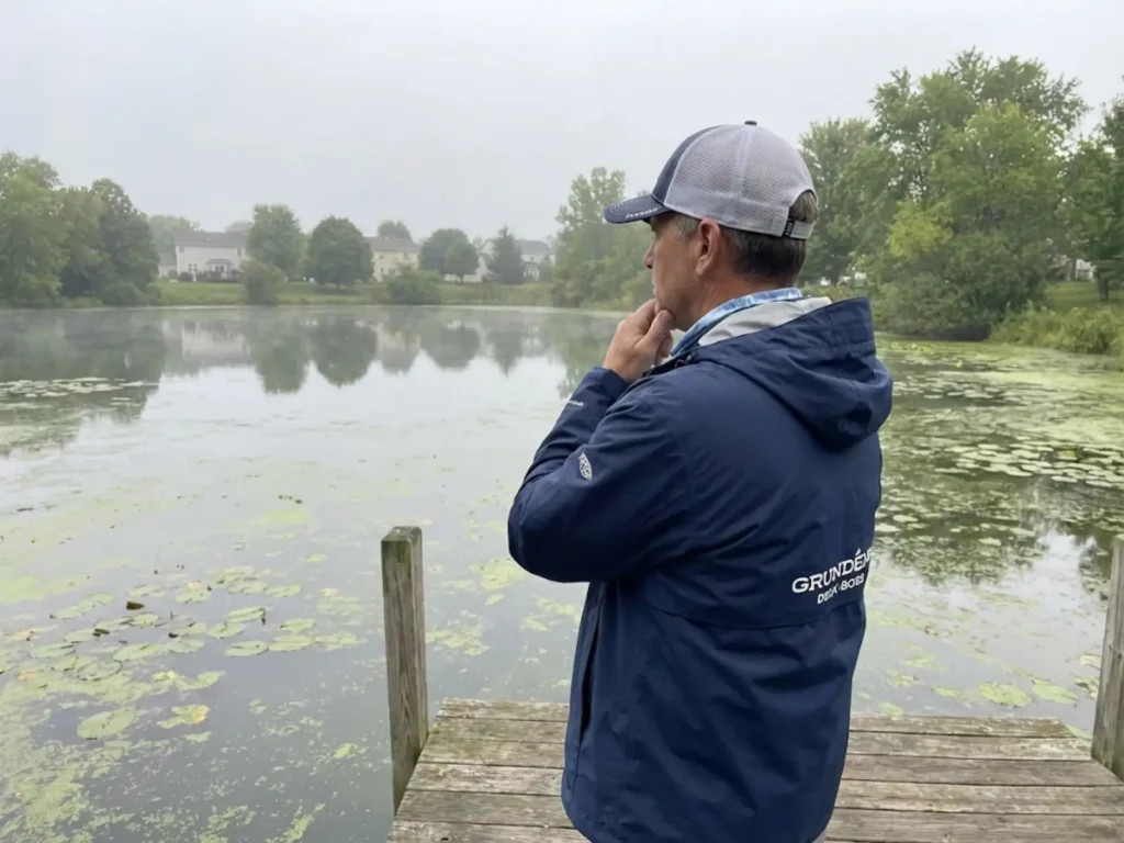 Experienced angler evaluating oxygen conditions at a small weedy pond at dawn